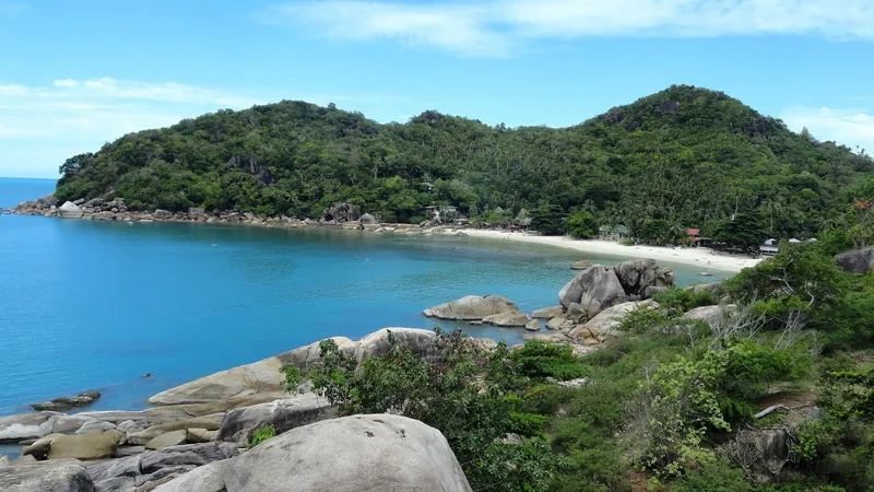 A secluded bay with turquoise water, granite boulders, and a forested headland at Thong Ta Kian Beach, Koh Samui.