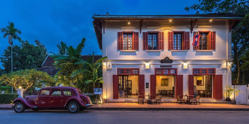 A vintage red car sits before a French colonial hotel lit up at dusk in Luang Prabang. A vintage red car sits before a French colonial hotel lit up at dusk in Luang Prabang.