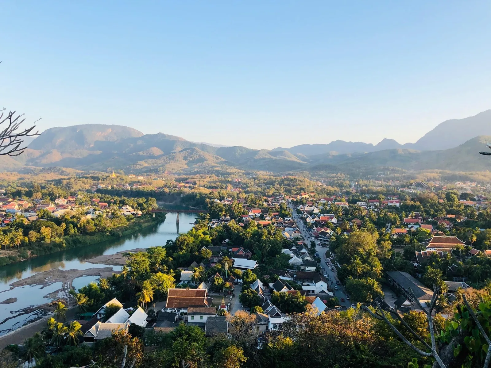 Aerial view over Luang Prabang's rooftops and river bend, framed by misty mountains at sunrise Aerial view over Luang Prabang's rooftops and river bend, framed by misty mountains at sunrise